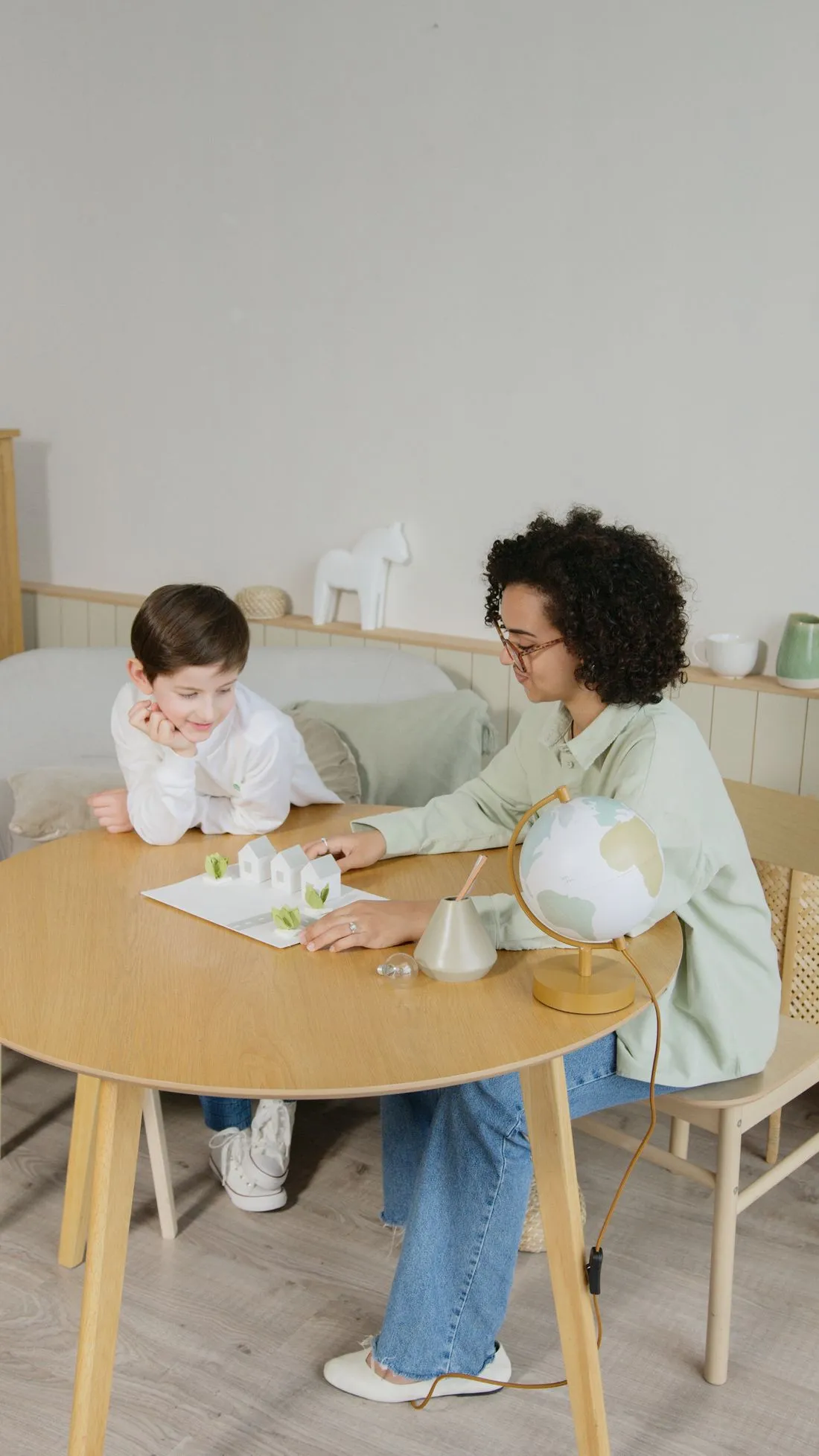 Mãe e filho estudando à mesa com maquetes de papel e um globo terrestre